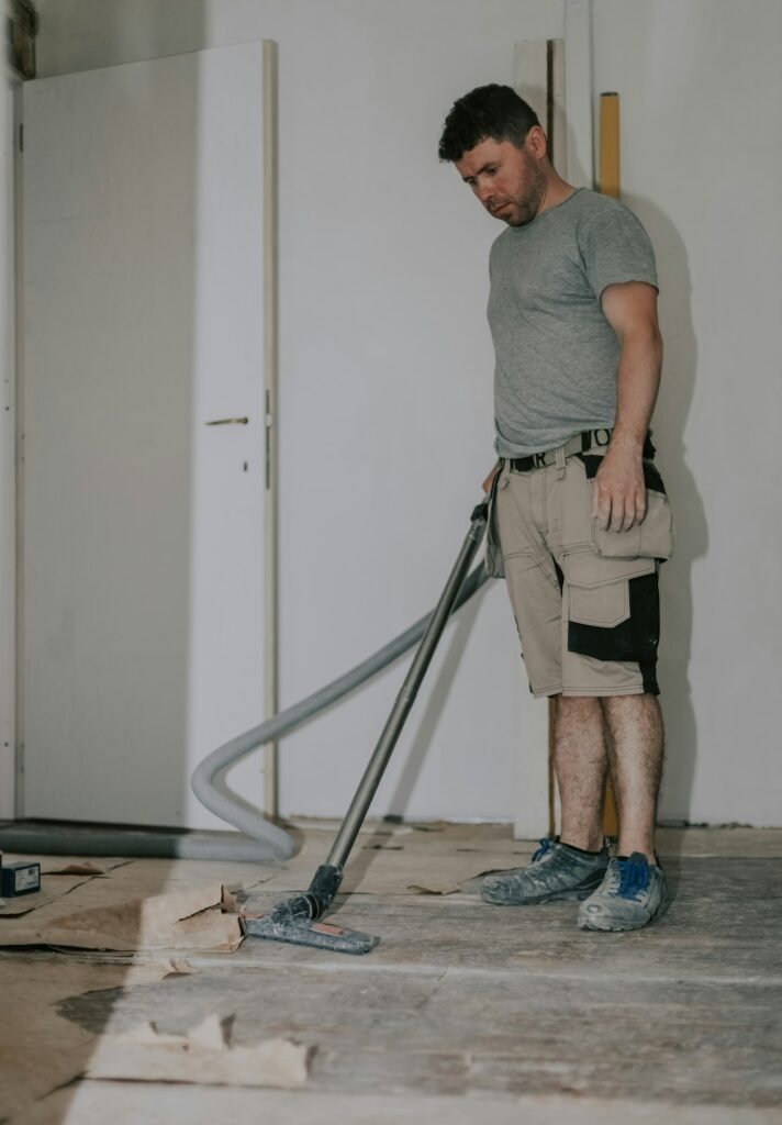 A young man vacuums the floor with a construction vacuum cleaner.