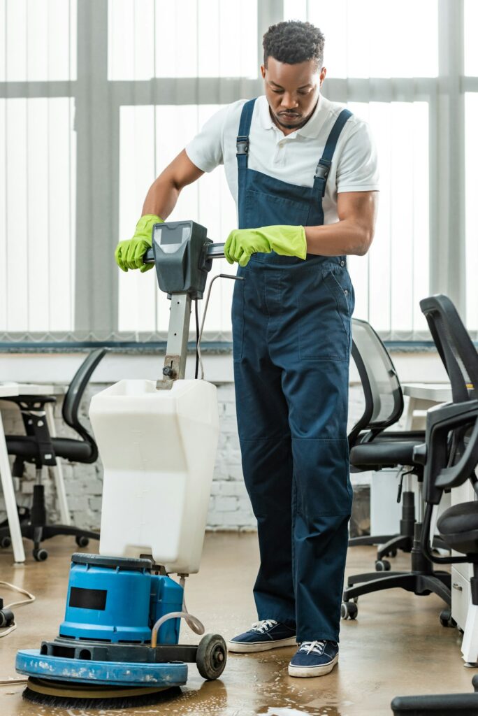 young african american cleaner washing floor in office with cleaning machine