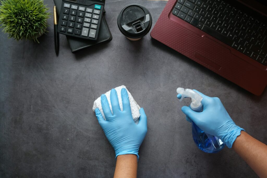 Gloved hands disinfecting an office desk with spray and a cloth